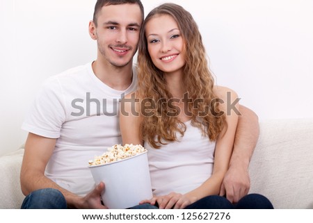 happy young couple sitting on the sofa eating popcorn and watching  tv