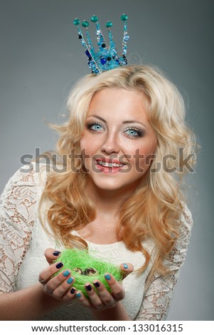 portrait of smiling woman wearing  blue princess crown and holding nest with quail eggs