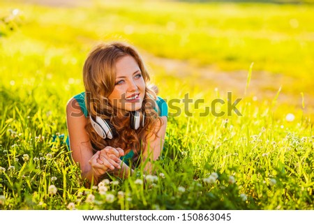 happy girl listening to music lying on the grass in the summer park, looking to the side