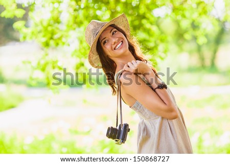 happy young girl wearing straw hat with vintage camera walking in the park and looking back, copy space from the left side