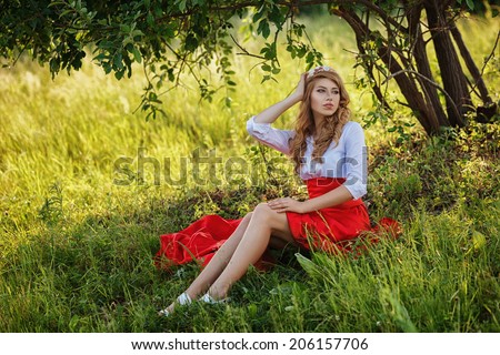 Romantic portrait of the woman in red skirt sitting under the tree