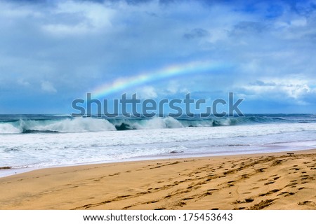 Rainbow over beach and waves hitting the shore, Kauai Hawaii