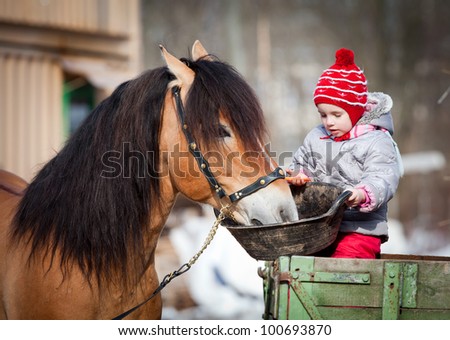 Child feeding a horse, sitting on a cart in the winter.