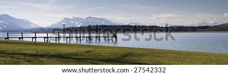 Two people sitting on the landing at the Chiemsee with the alps in the background. Panorama picture