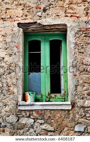 Decayed window with paint bucket on window-sill, broken glass and stone wall
