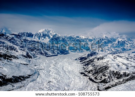 Aerial View of Alaskan Glacier Leading up to Mt. McKinley, Spewing Out Snow and Clouds.  The Great Alaskan Wilderness, Denali National Park, Alaska.  A Beautiful Snowscape of Rock, Snow, and Ice.