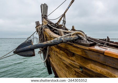 Anchor, wooden planks, ropes, pulleys, tackle, and rigging of an old replica of a 1400\'s era sailing ship.