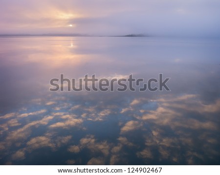 Morning sun rises over misty river with golden clouds reflections