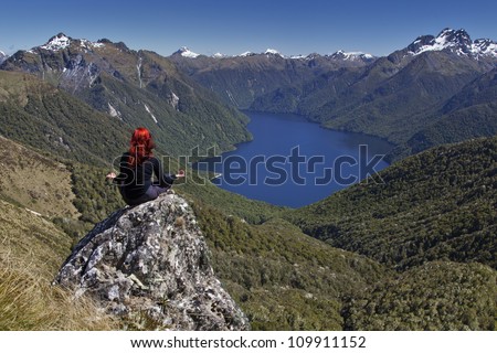 Red haired woman doing yoga overlooking lake and snow capped mountains.