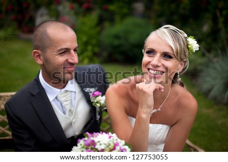 Smiling handsome groom looking at his beautiful blond bride in the garden with wedding bouquet.Happy, laughing, just married.
