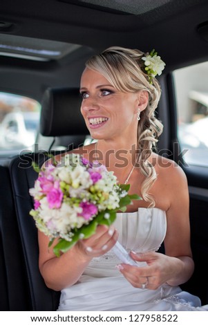 Beautiful blond bride smiling sitting in the car with her wedding bouquet of white roses and pink lilies.