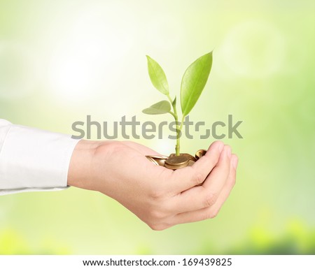 Businessman holding plant sprouting from a handful of coins