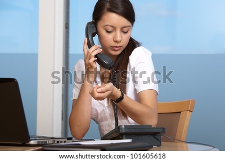 Attractive young woman in office talking on phone looking at watch