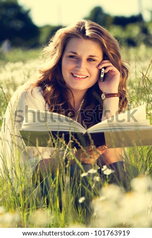 Vintage looking shot of beautiful young woman in field holding phone and book.