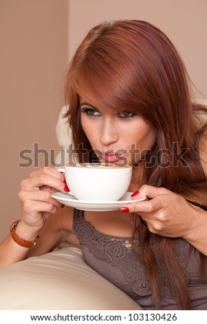 Beautiful woman at home relaxing on sofa sipping cappuccino