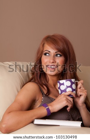Beautiful woman at home sitting on sofa relaxing with drink. Copy space above head.