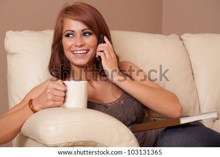 Beautiful woman at home relaxing with drink, a book and talking on phone