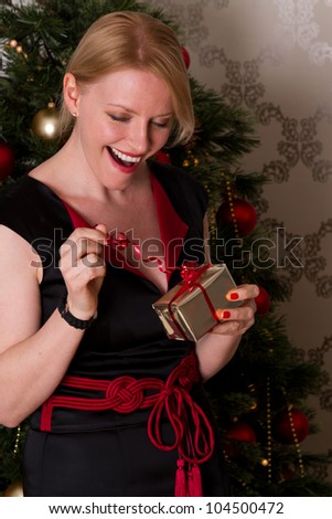 An excited smartly dressed woman pulling ribbon on Christmas present