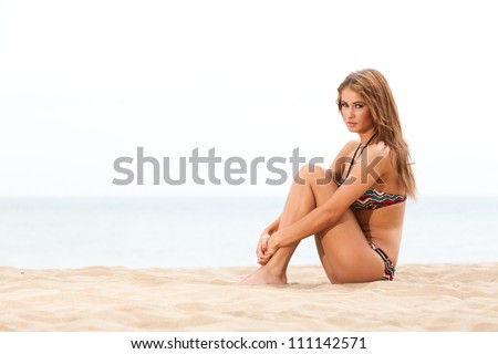 Young woman sitting on beach in bikini sun bathing