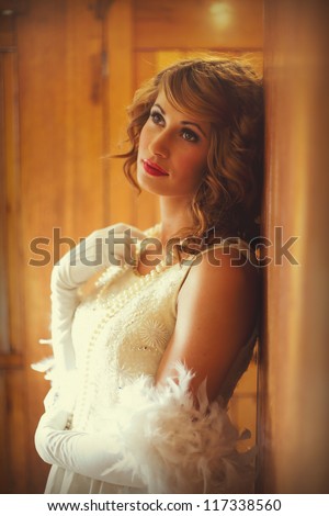 Beautiful woman in 1920s flapper dress standing in a train carriage leaning against wood panelling