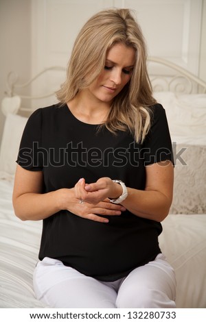 Young pregnant woman with hand on tummy looking at watch and timing contraction pains