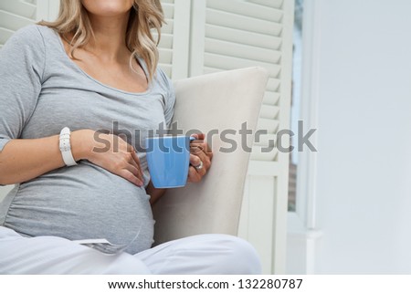 Close up of unrecognisable pregnant woman sitting on chair holding blue mug, copy space included