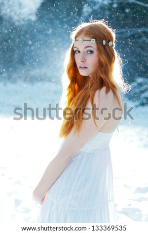 Snow Maiden. Fantasy image of beautiful red head woman standing in snow, looking at camera