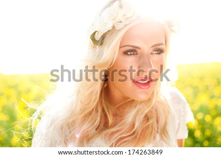 Fashion image of beautiful woman in rapeseed field, wearing flowers in hair