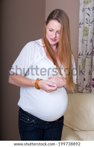 Pregnant woman standing in pain and resting hands on her tummy timing contraction pains