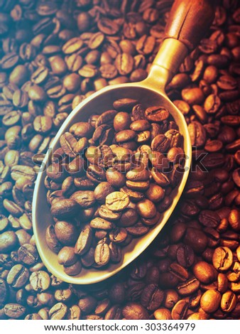 brass scoop with whole coffee beans on a coffee beans background.Filtered image: cool cross processed vintage effect.