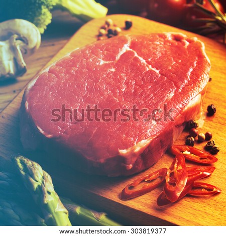 Raw Steak with green asparagus on wooden board. Filtered image: warm cross processed vintage effect.
