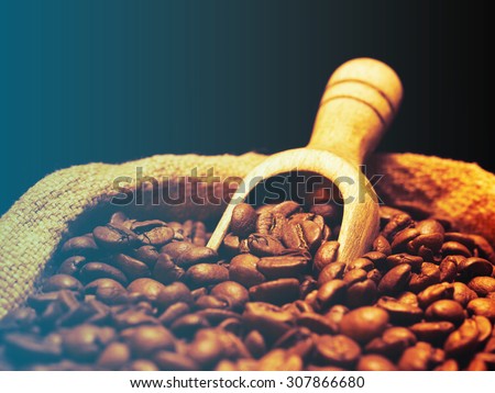 Coffee beans on burlap sack with wooden scoop.Filtered image: cool cross processed vintage effect.