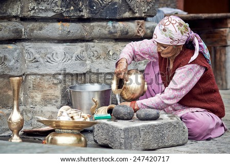 Naggar, INDIA - JULY 17: Old Indian woman cleans the dishes out of the temple. Special dishes which make offerings to God in the temple. July 17, 2013 in Naggar, Kullu Valley, Himachal Pradesh, India.