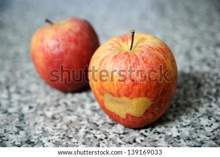 Two red apples, one of them with a peculiar mark on it.