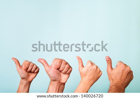 Four hands making thumbs up gesture. Success team on blue background. The hands have different skin tones.