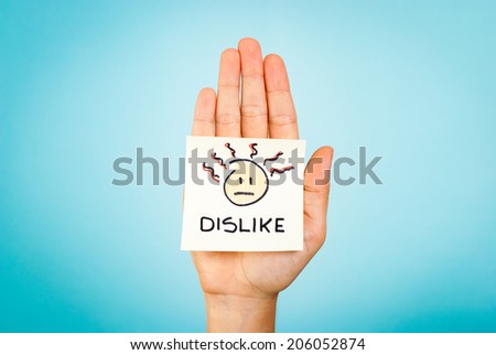 The word dislike and emoticon/emoji stick note on the palm of the hand up, with blue background. Bad feelings, not agree.