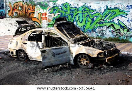 Burnt out car in front of a wall with graffiti.
