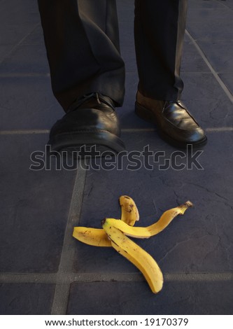 A man with black shoes about to step on a banana peel.