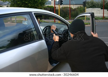A robber dressed in black pointing a gun at a driver in a car.