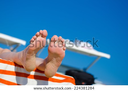 Sandy feet of woman sunbathing at the beach on a deck chair with white orange striped towel.