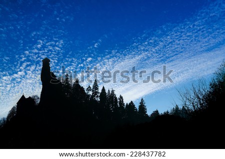 Dark ancient castle silhouette on a hill covered with trees and with dramatic deep blue cloudy sky