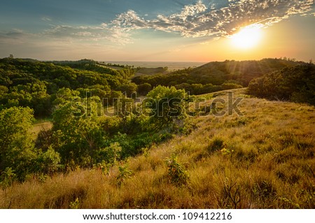 Sun peaking under clouds at sunset over rolling hills