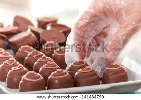 Saleswoman arranging chocolate truffles with vinyl glove on market