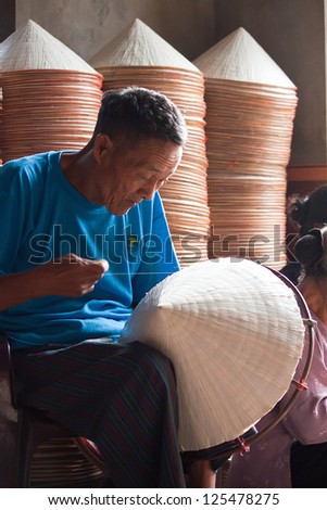 HANOI, VIETNAM - OCTOBER 23: Vietnamese man sitting sewing hats in a traditional village in Vietnam October 23, 2010. Conical hat is an traditional item of ethnic Vietnam