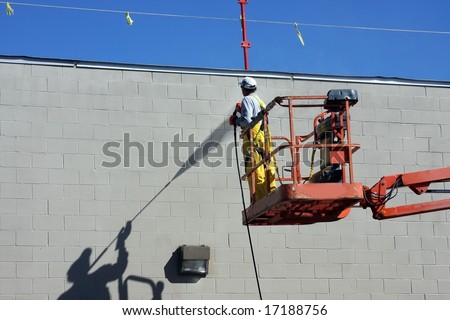 worker and his shadow pressure wash a building