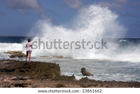 angry seas crash waves in front of a woman in a swim suit