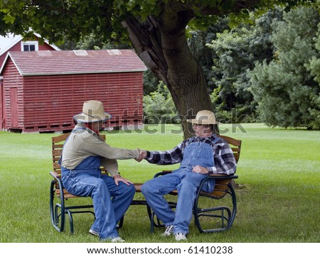 two farmers in bib overalls shaking hands sitting in lawn chairs