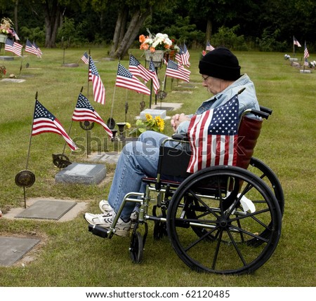 disabled war vet in a wheelchair holding american flag at a grave site
