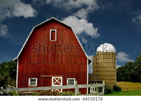 vintage red barn and silo with a white fence against a blue sky