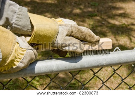 worker with gloves on wire brushing a chain link fence